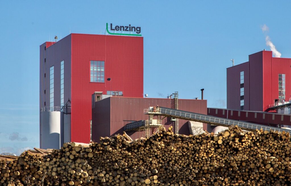 Lenzing Biocel Paskov Areál Lenzing Biocel Paskov s červenými výrobními budovami a zásobou dřevní suroviny v popředí.