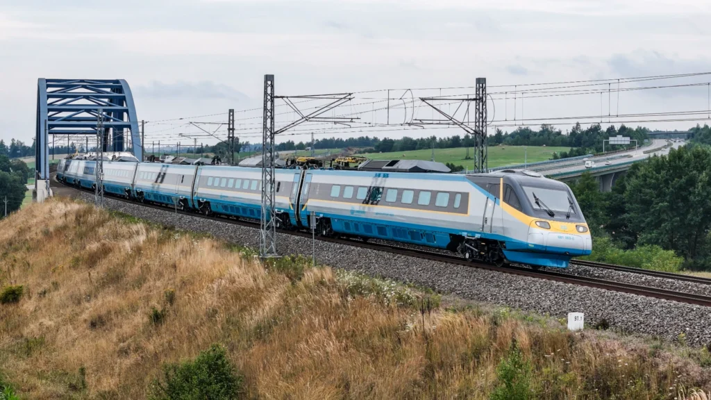 Pendolino Českých drah projíždí po trati přes most v otevřené krajině