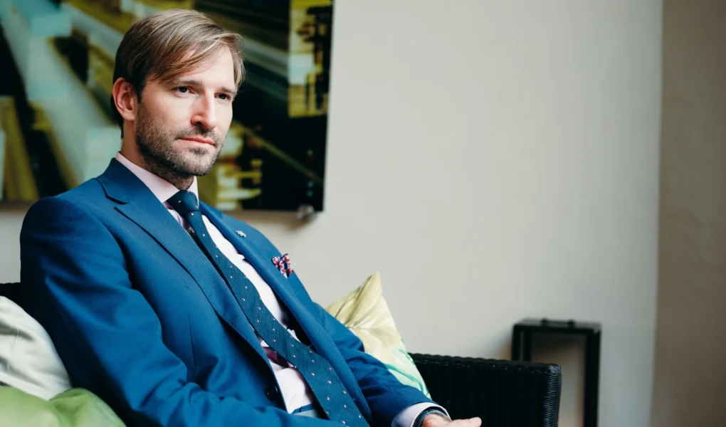 Ministr Adam Vojtěch v modrém obleku sedí v interiéru a dívá se mimo záběr.