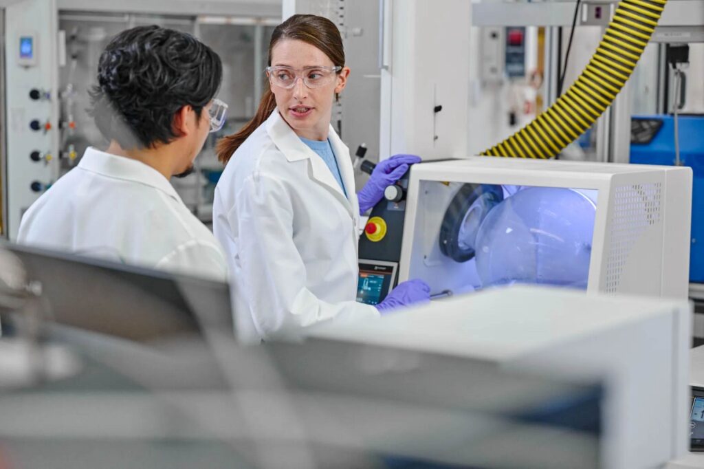 Boehringer Ingelheim researchers in the lab Two Boehringer Ingelheim employees in lab coats and safety goggles discussing a production process at laboratory equipment.