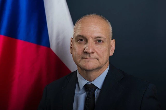 Václav Bartuška, Ambassador of the Czech Republic to the United Kingdom, in an official portrait with the Czech flag in the background.