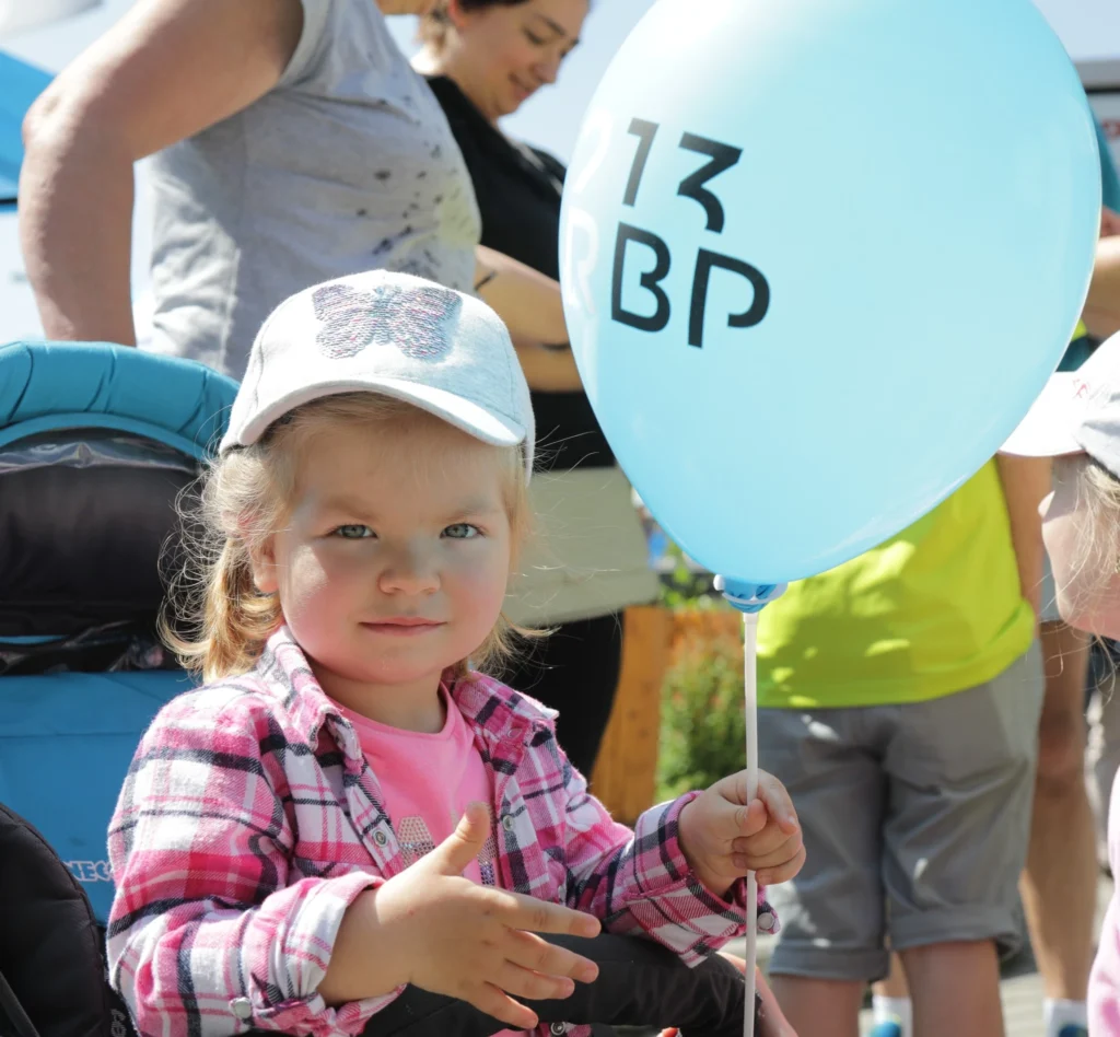 Malá holčička drží světle modrý balónek s nápisem RBP 213 na venkovní akci.