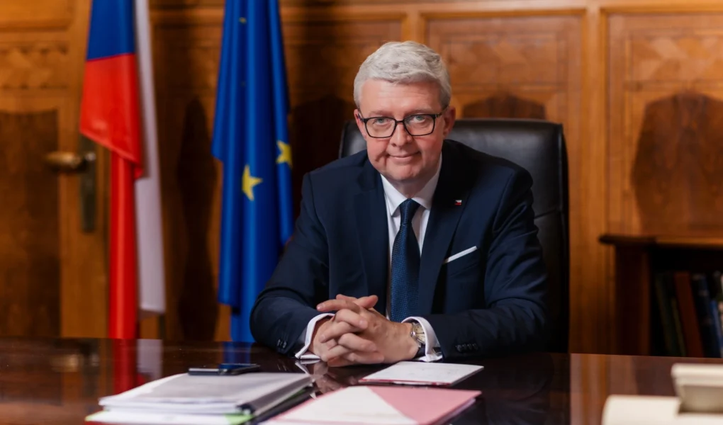 Ministr Karel Havlíček sedí za pracovním stolem v kanceláři, v pozadí jsou česká a evropská vlajka.