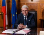 Ministr Karel Havlíček sedí za pracovním stolem v kanceláři, v pozadí jsou česká a evropská vlajka.