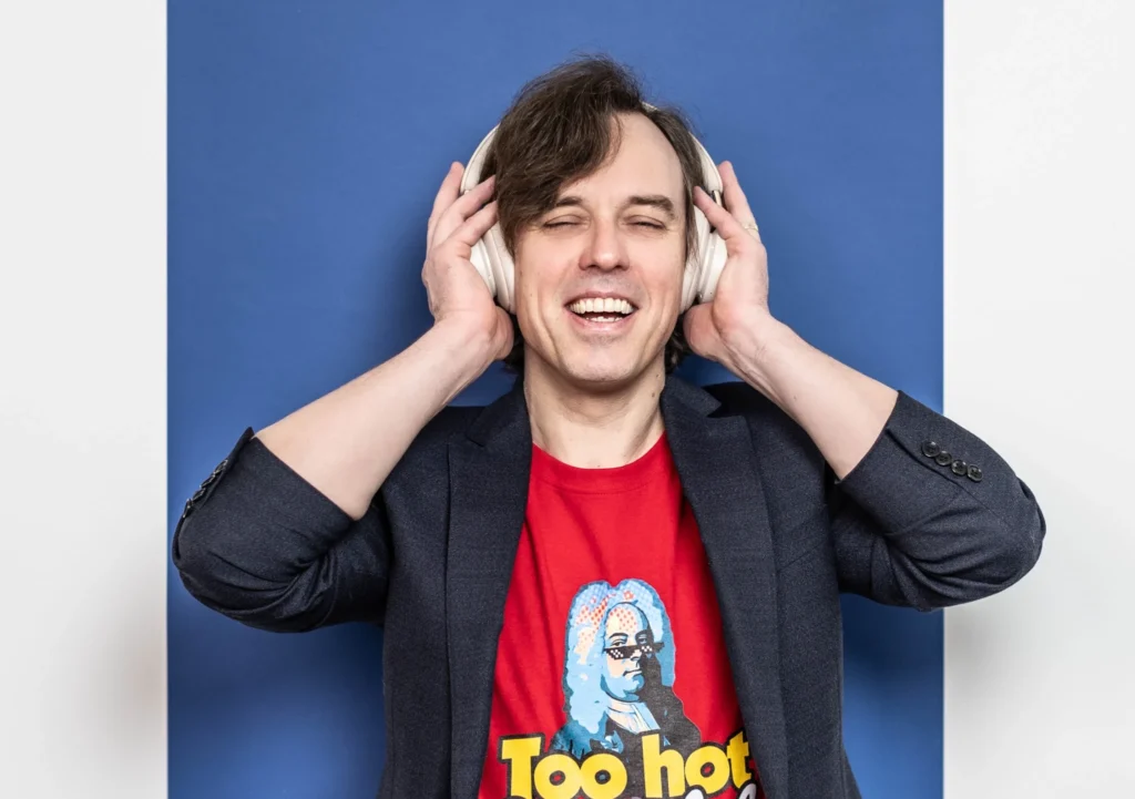 Festival Krumlov dramaturge Martin Rudovský wearing headphones in front of a blue background.