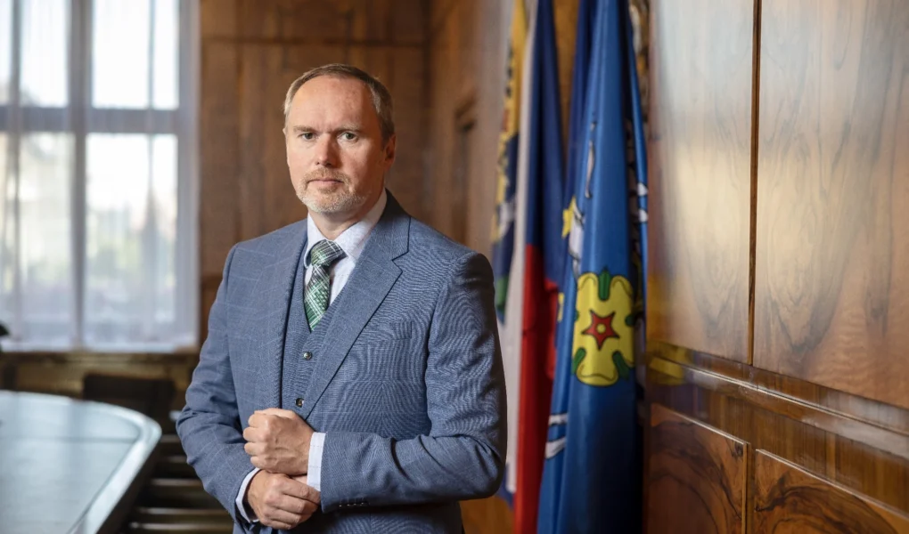 Náměstek primátora Ostravy Břetislav Riger stojí v reprezentativním interiéru magistrátu, v modrém obleku před vlajkami.